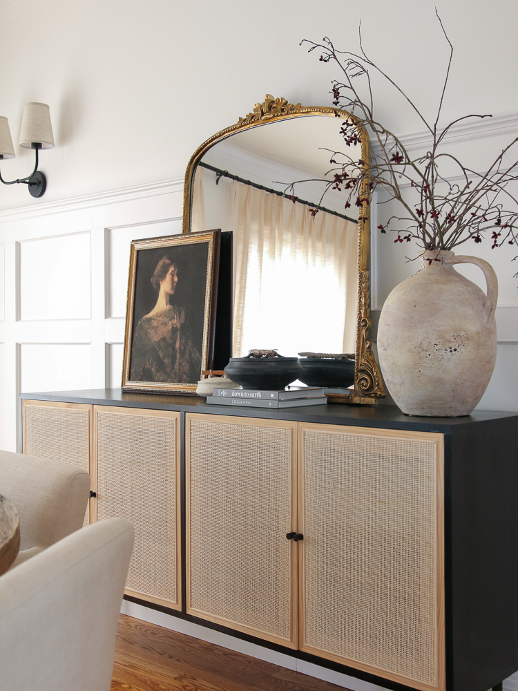 dining room with sideboard and wall sconces to fill a big blank wall, gleaming primrose mirror , artwork, vase with stems, coffee table books and trinket dishes styled on sideboard
