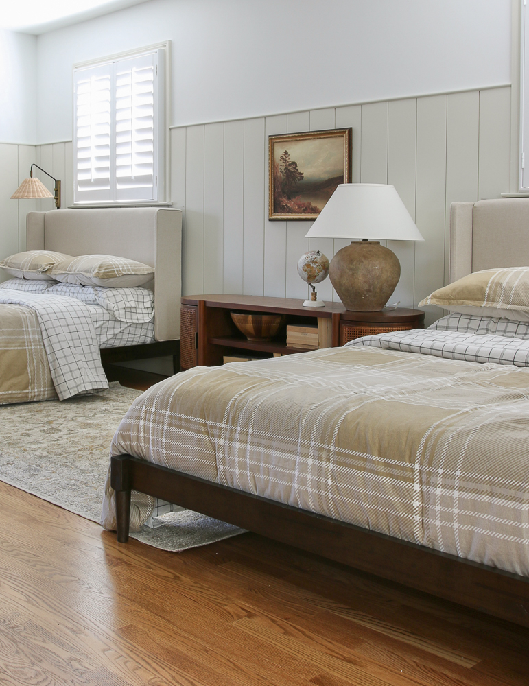 shared boys room with vertical shiplap, two upholstered beds, console table and lamp between beds, hardwood floors