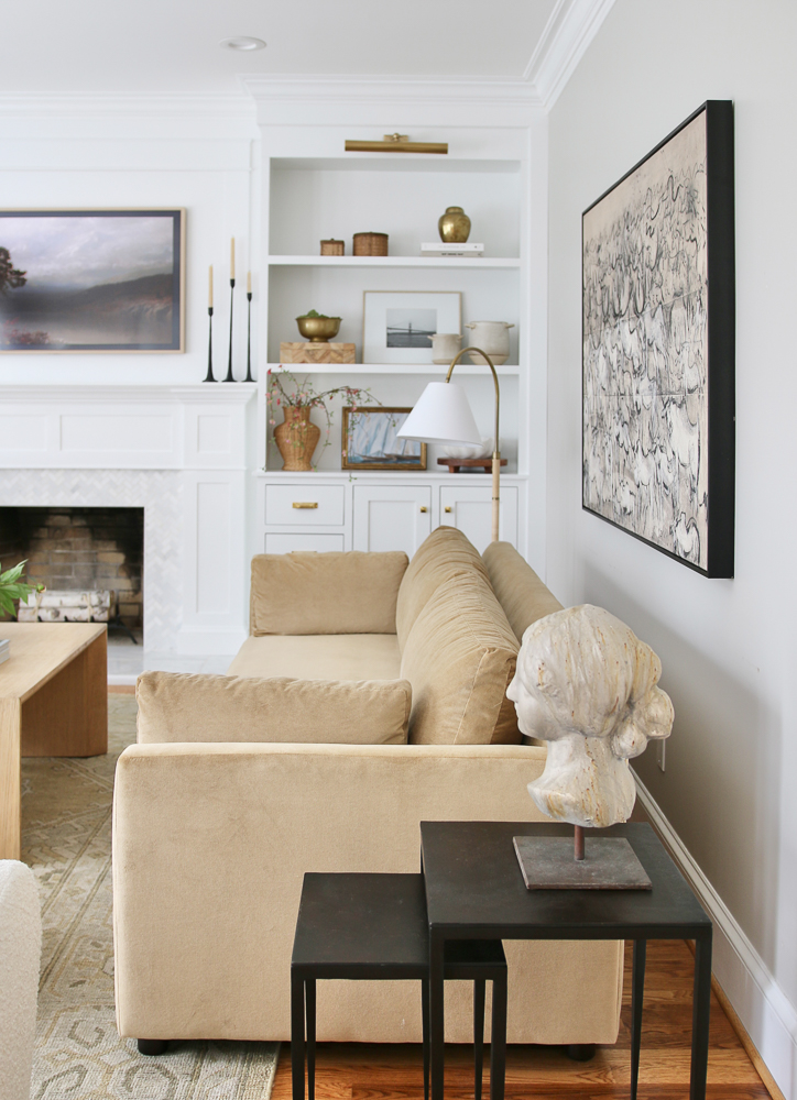 side view of living room showing large wall art over sofa, white built-in shelves, nesting tables