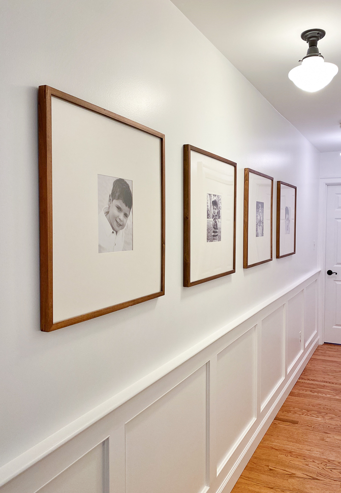 long hallway painted pure white with wall molding and framed gallery wall with photos