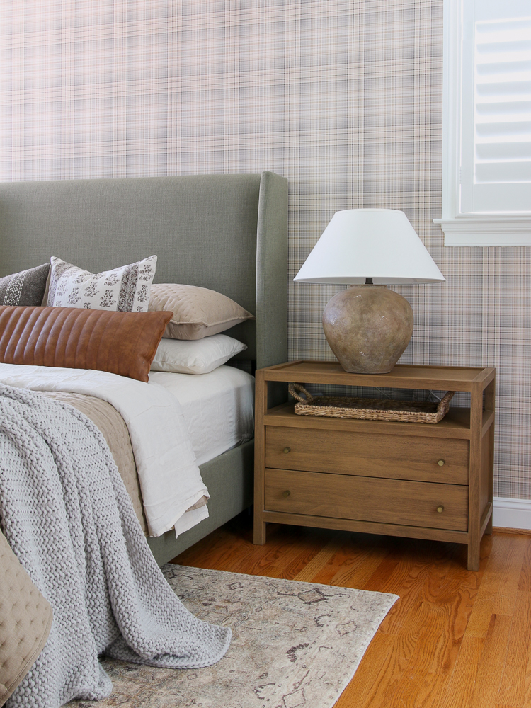 neutral plaid wallpaper with upholstered bed, wood nightstand, lamp, interior window shutters
