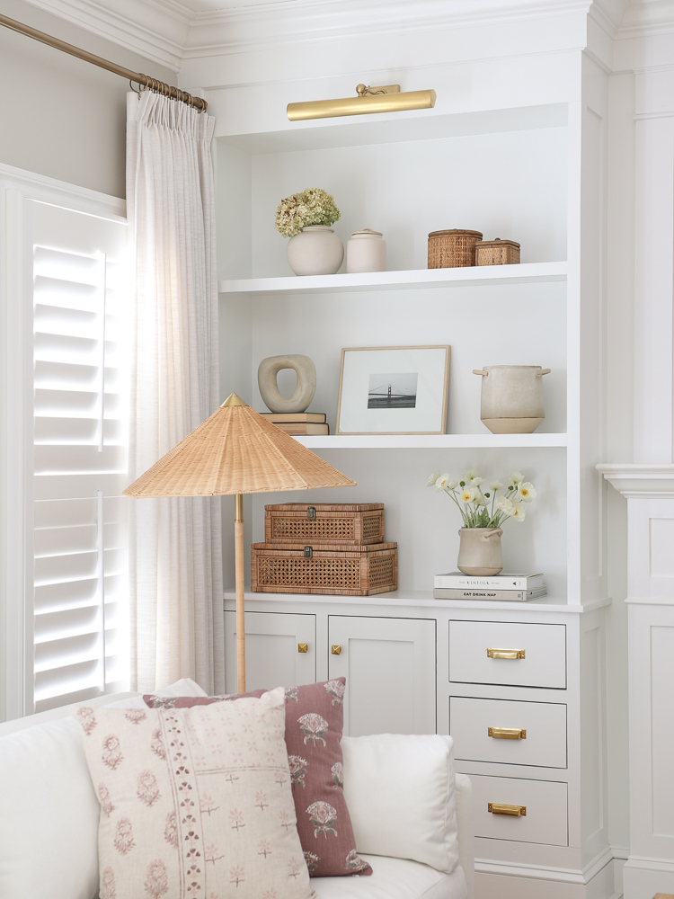 white living room built-in shelves styled with home decor, rattan lamp, white velvet sofa