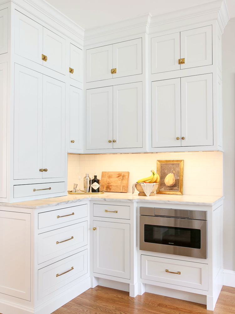 White kitchen cabinets with under cabinet lights on, microwave drawer, brass hardware