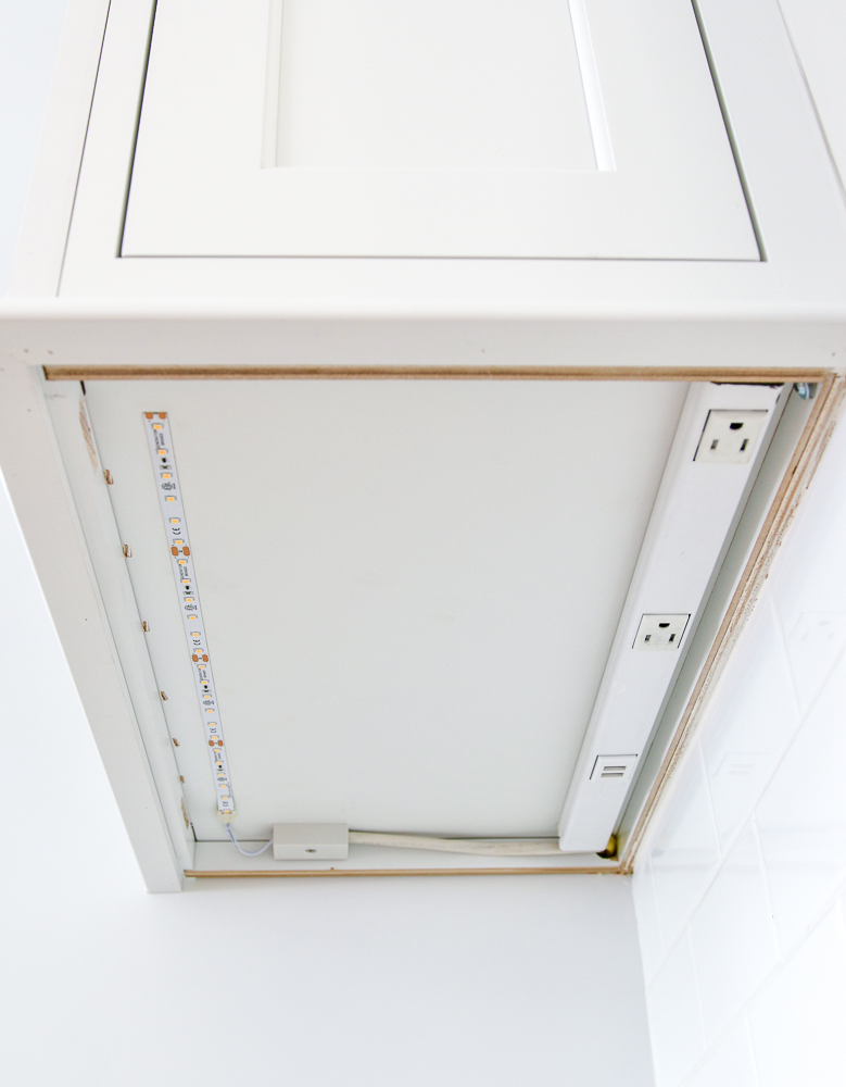 under side of white kitchen cabinets showing LED strip lights and power strip hardwired and mounted under cabinet