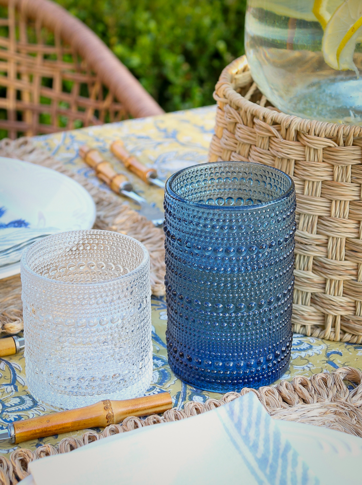 close up of outdoor drink ware, beaded vintage-style hobnail blue and clear cups next to beverage dispenser
