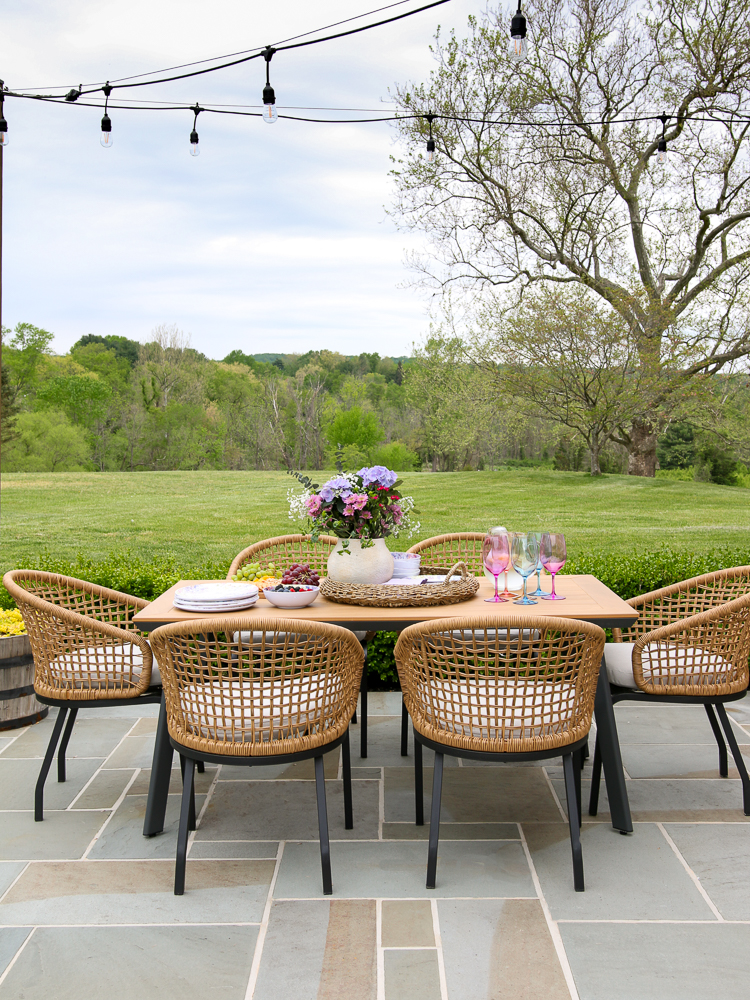 rectangular patio dining table with woven outdoor chairs, string lights above dining area of outdoor entertaining area