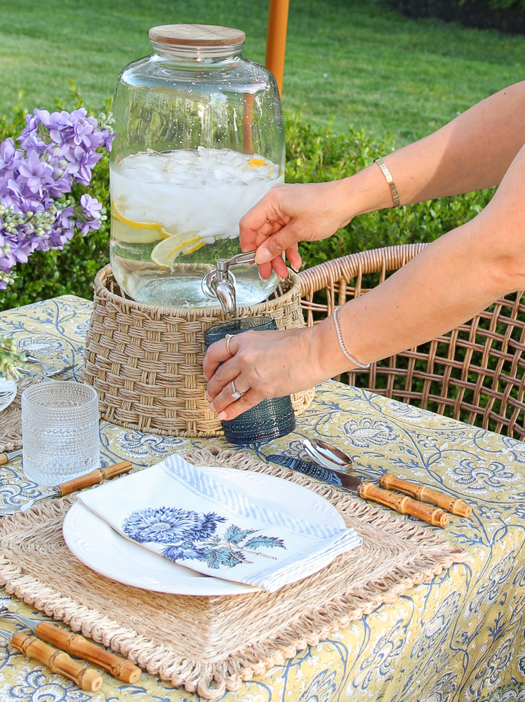 Stefana Silber using beverage dispensers to fill a blue outdoor beaded cup, outdoor tablescape