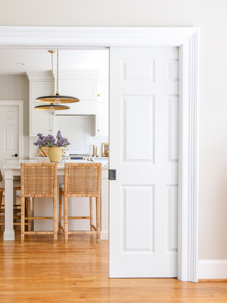 double pocket door with right side partially closed, view into classic white kitchen with hardwood floors