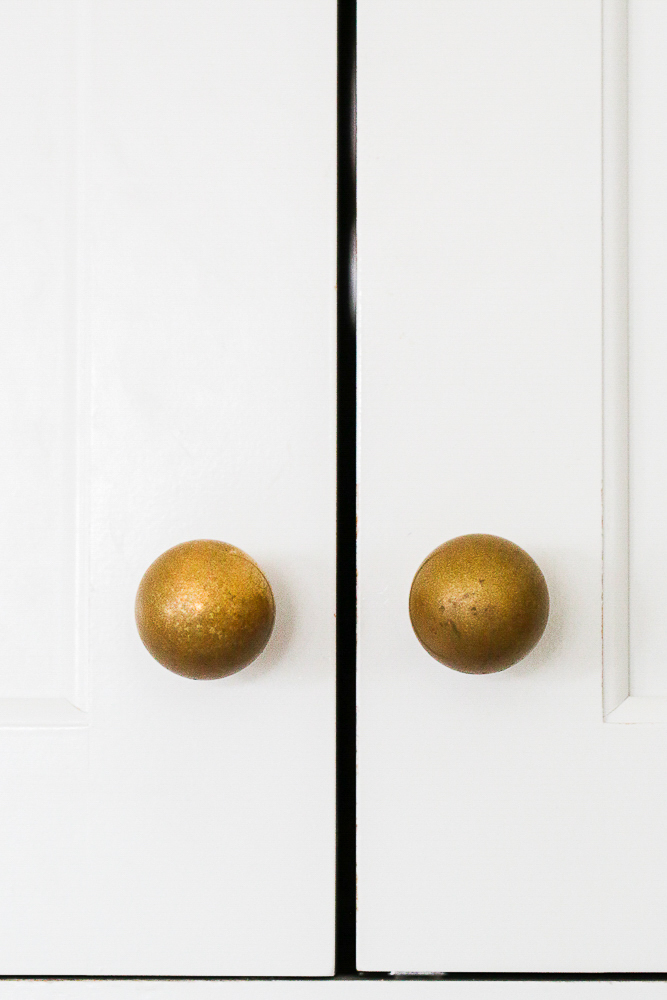 close up of unlacquered brass hardware with heavy tarnish, white cabinets