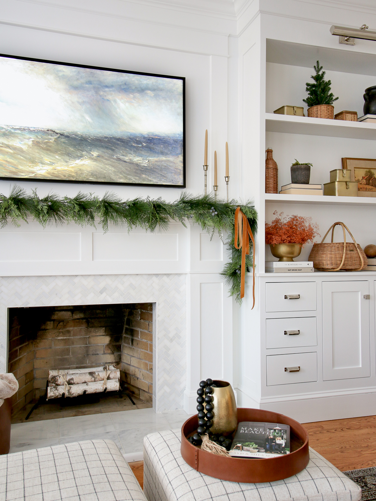 frame tv above fireplace with garland on mantel. Shelf decor on builtins next to fireplace