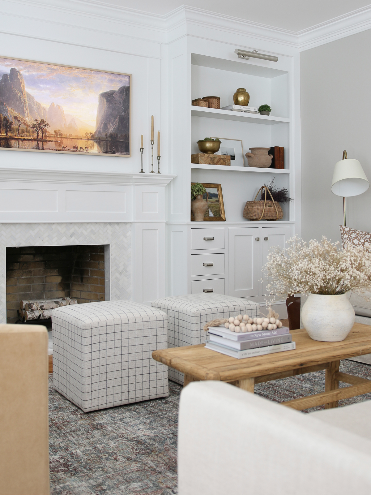 Frame TV above the fireplace with white builtin shelves on each side. Oriental rug with vintage wood coffee table