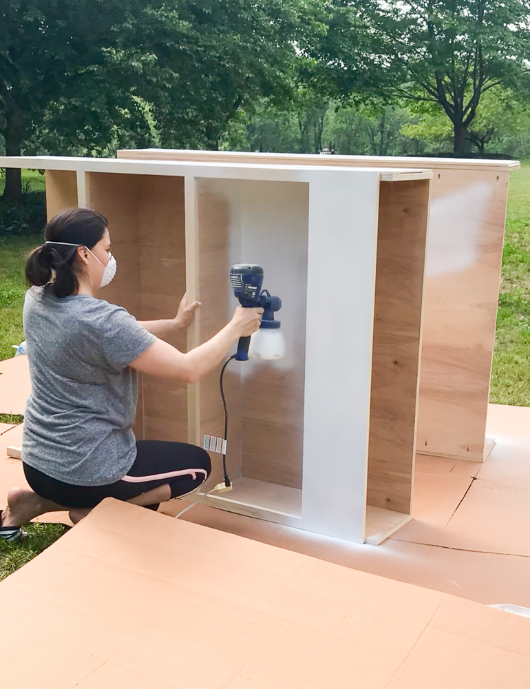 Stefana Silber painting DIY cabinet frames with sprayer outdoors