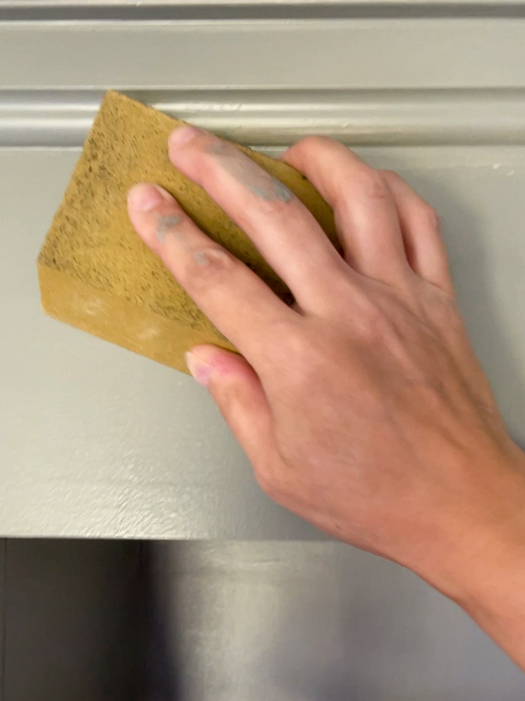 person sanding between coats of paint with sanding sponge