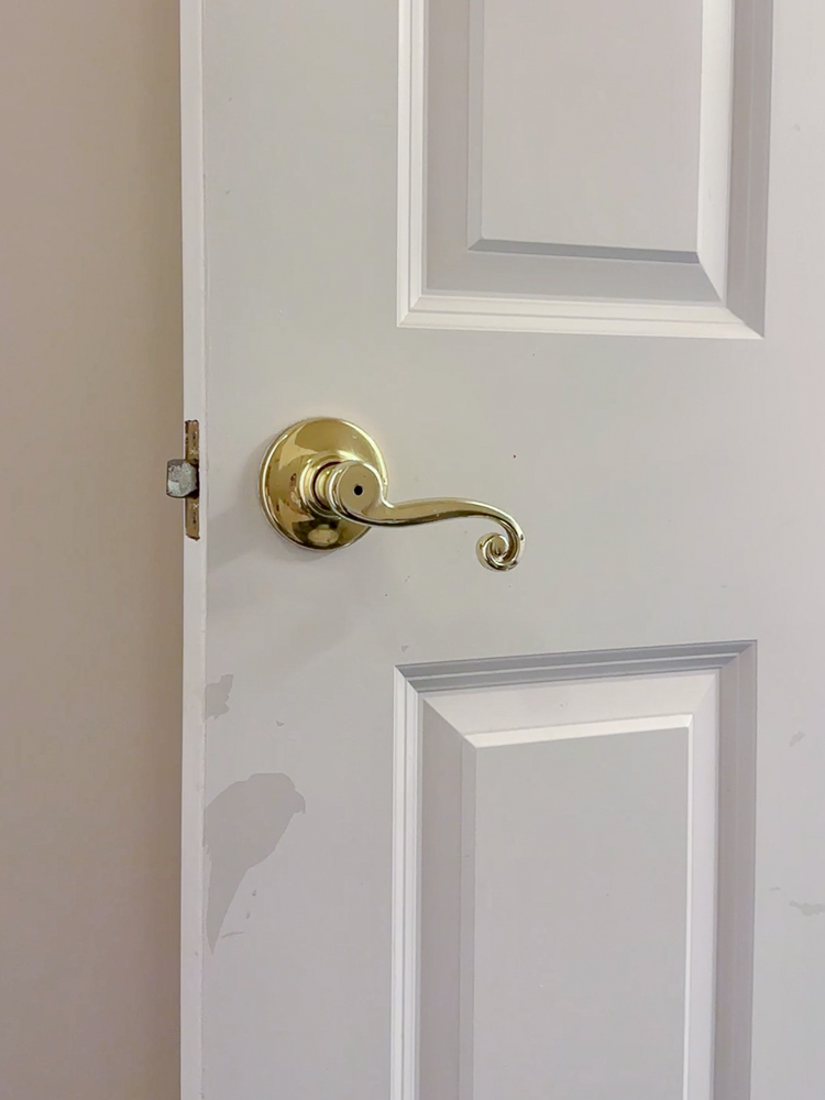 90s home interior, white door with painted gold hardware, water-based paint peeling off previously oil-based painted surface