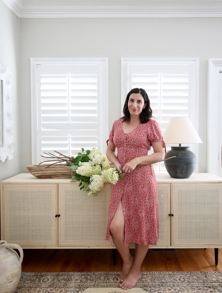 Stefana Silber standing in front of cane cabinet she made. Cabinet decorated with fresh cut hydrangeas and Pottery barn lamp.