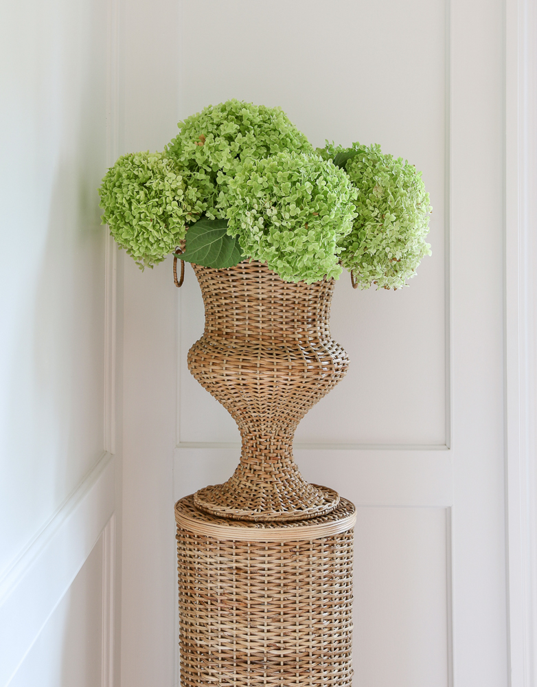 rattan urn and pedestal styled with fresh cut hydrangeas in an entryway with wall molding