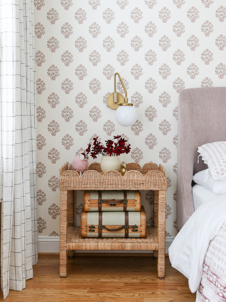 Girls bedroom with block print wallpaper, wicker side table, mauve velvet bed, demonstrating decorating trends using wallpaper