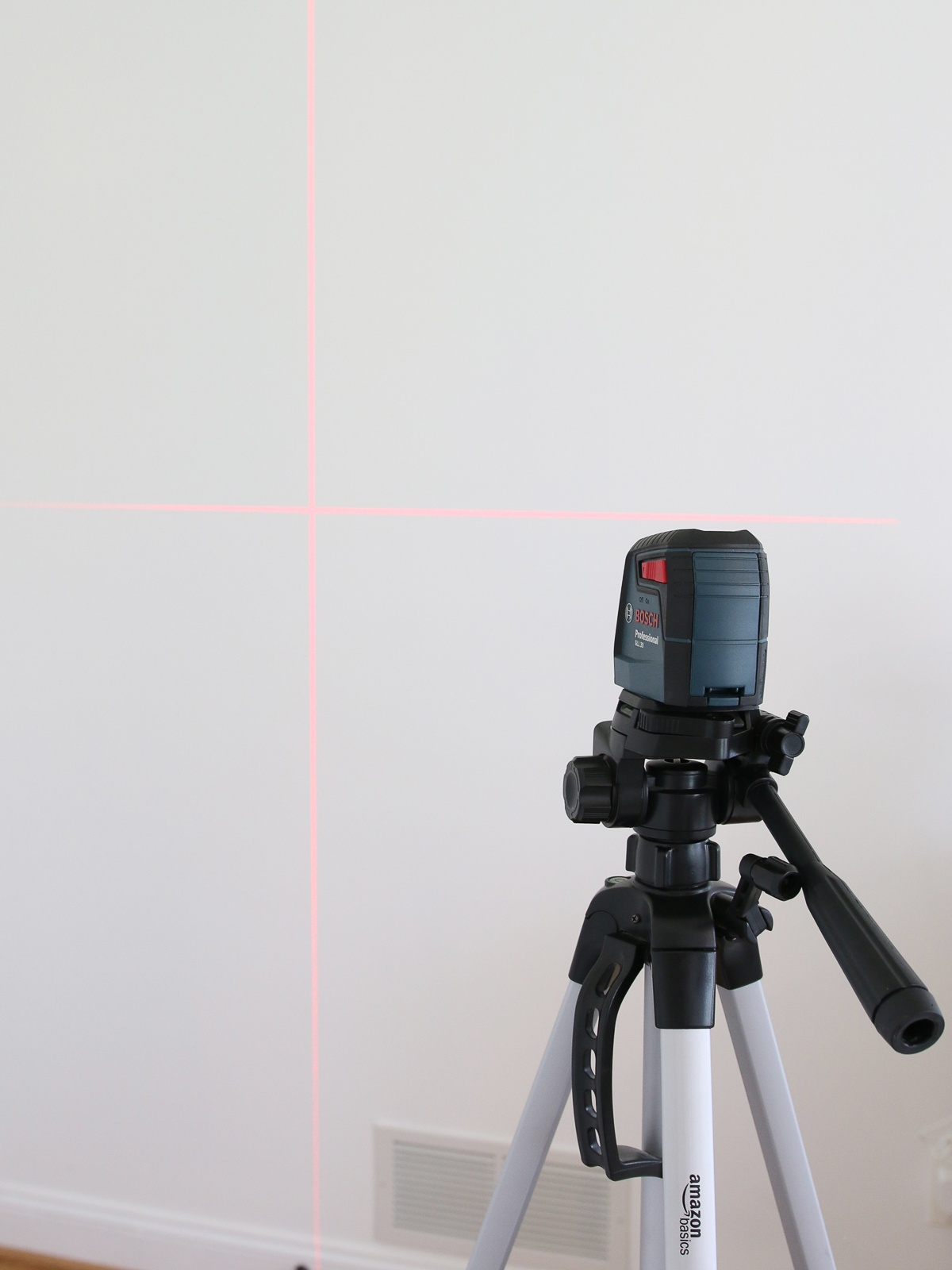 Laser level on a tripod creating a plumb and level line on a white wall