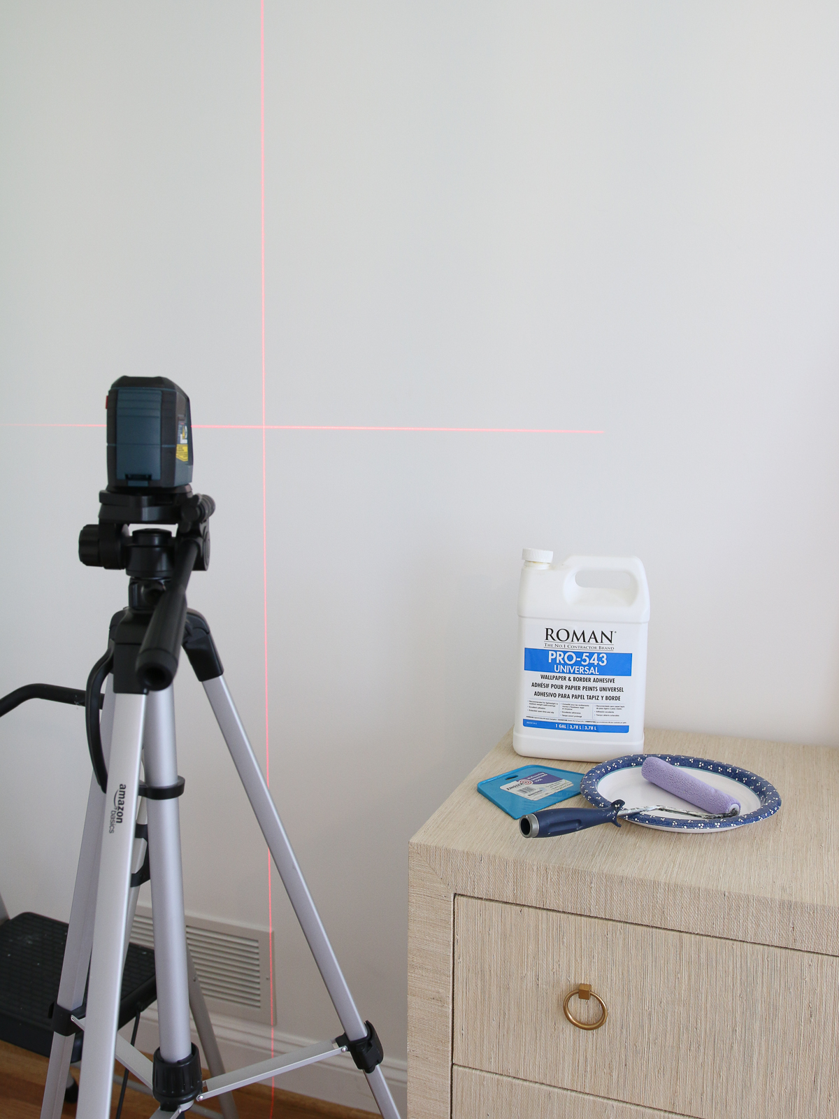 supplies for hanging wallpaper - laser level on a tripod, wallpaper paste, smoothing tool, paint roller