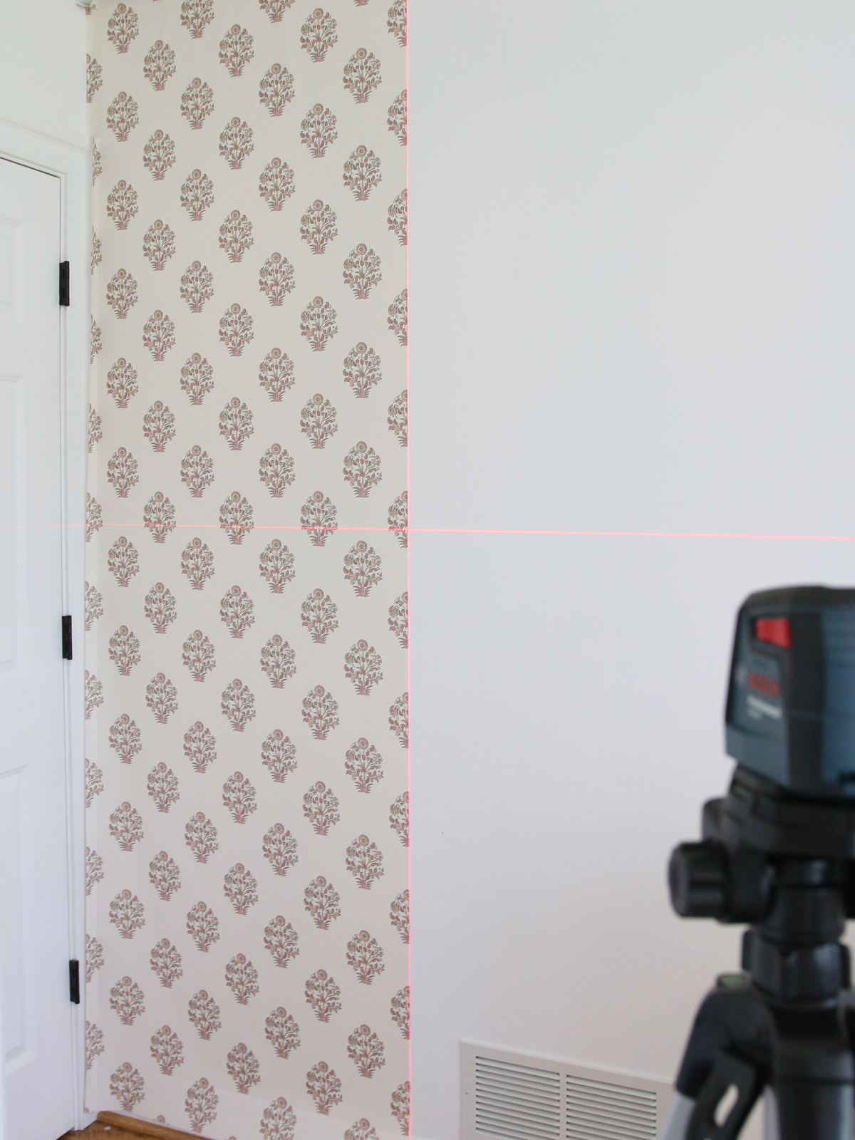first strip of wallpaper in a corner with a laser level plumb line