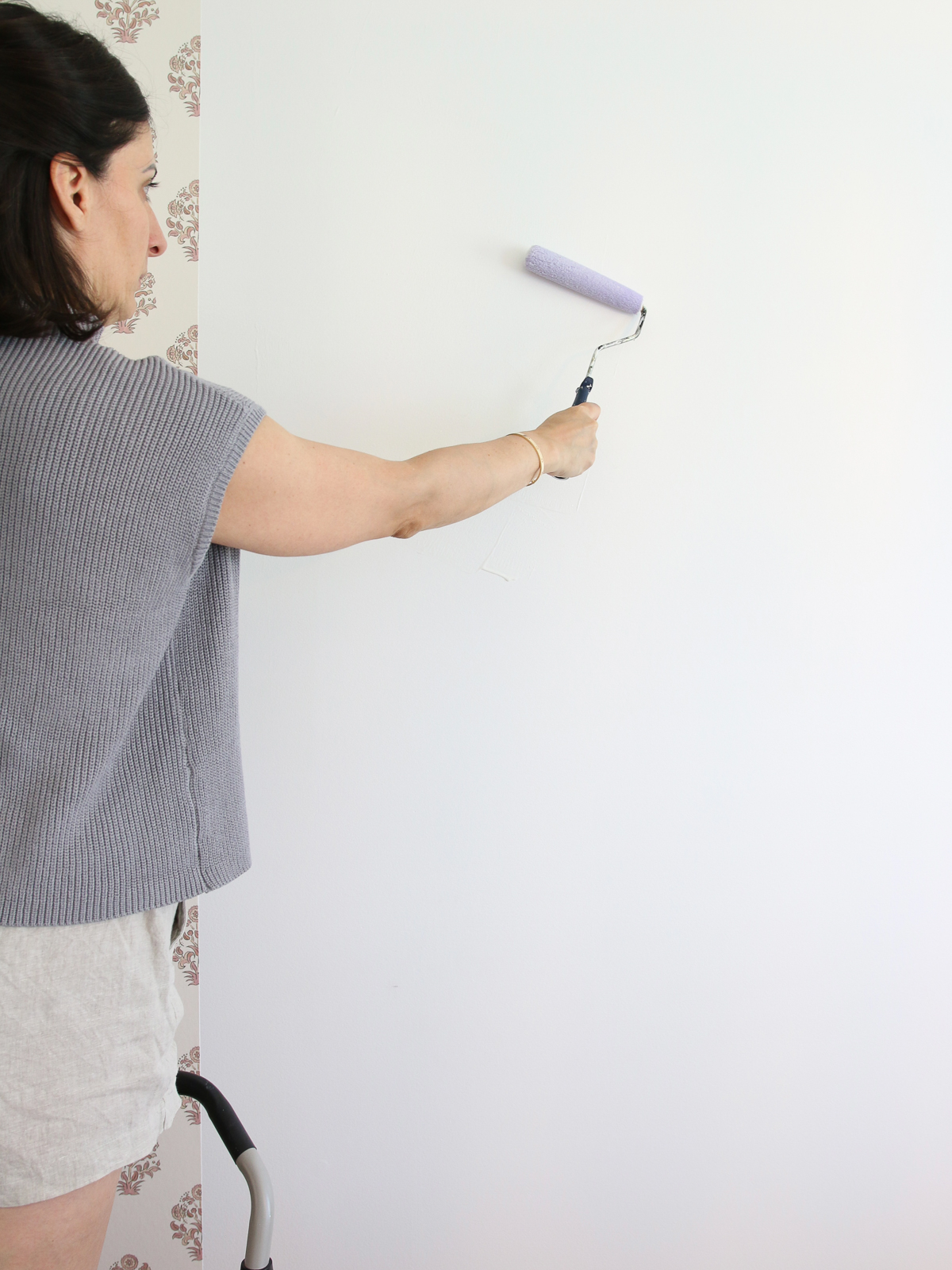 Stefana Silber rolling wallpaper paste with a paint roller on a wall