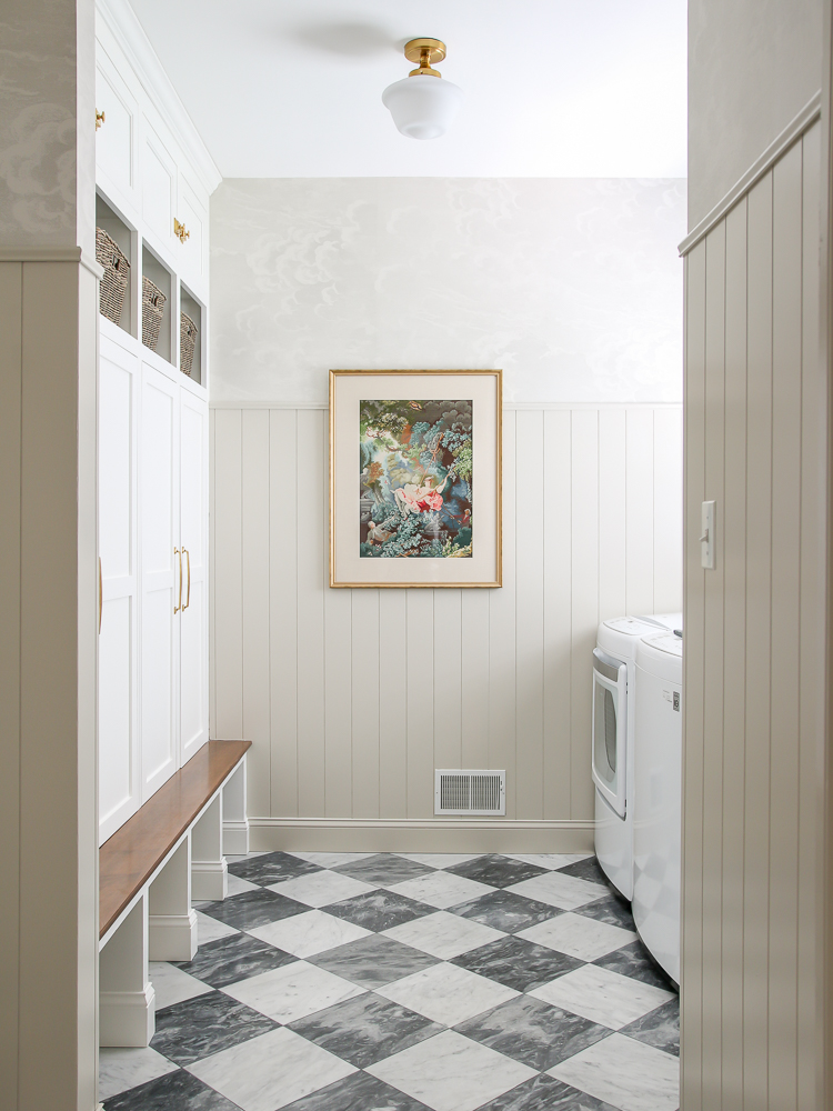 Mudroom and laundry room with gray and white marble checkerboard floor, vertical shiplap, neutral nuvolette wallpaper,  builtin cabinets, brass cabinet hardware, walls painted Accessible Beige