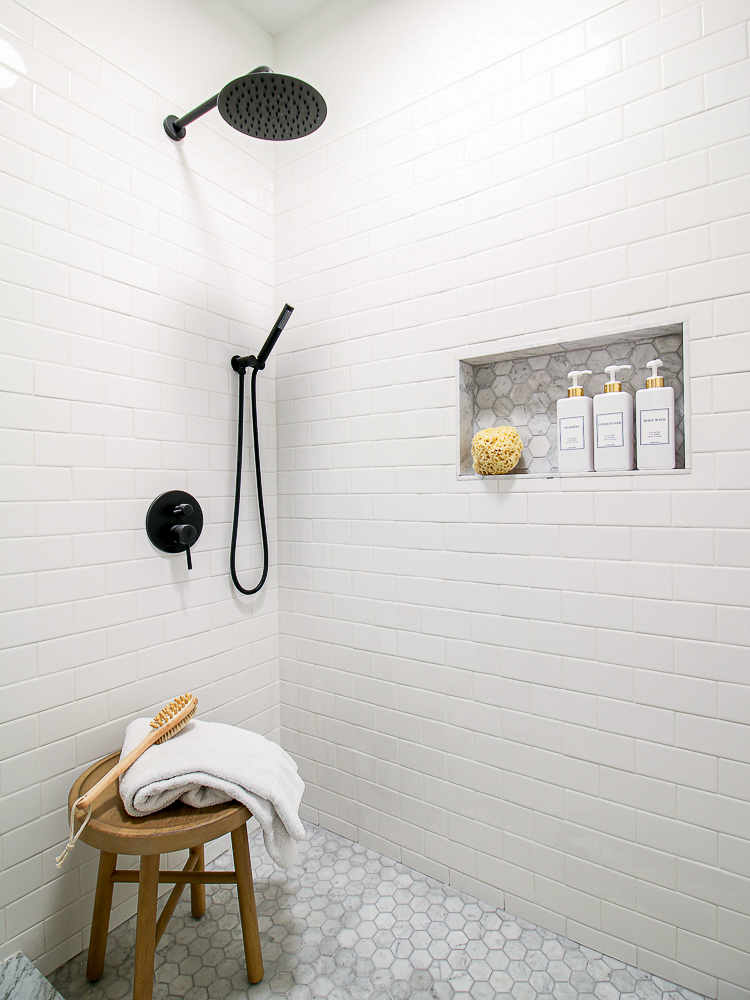 who subway tile shower with shampoo and conditioner niche, white refillable bottles, black shower fixtures, hexagon marble floor tiles. 