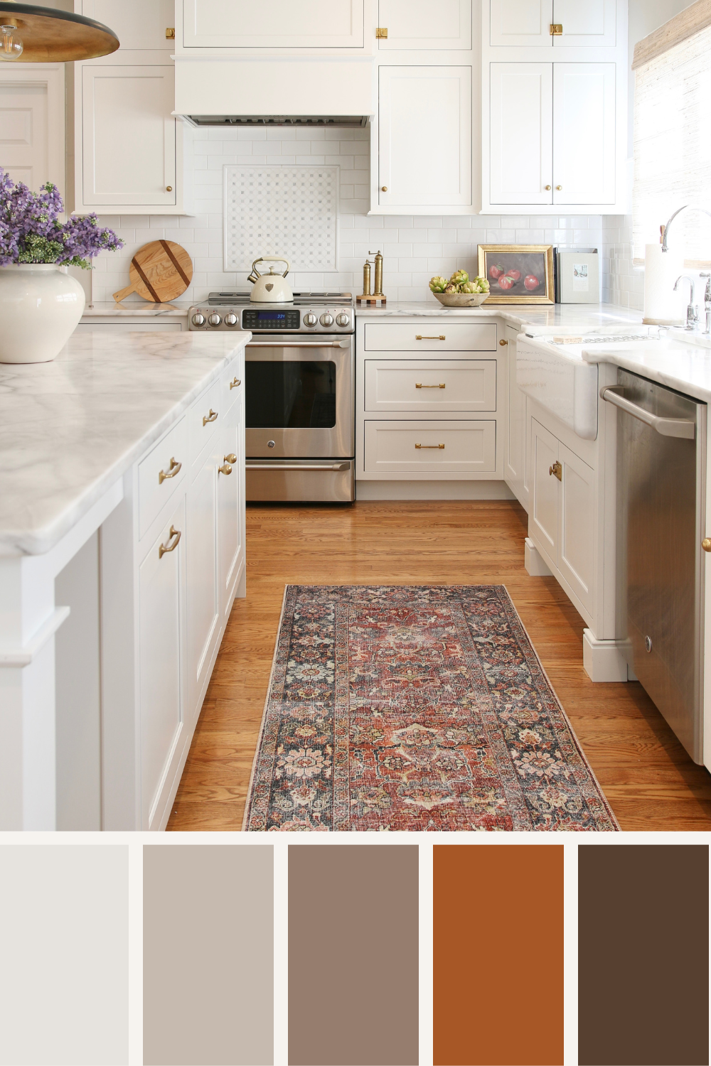 classic white kitchen with honed marble countertops, unlacquered brass cabinet hardware, fall accents throughout space, bowl with artichokes and still life apple artwork on counter, kitchen runner rug with fall colors, rustic red tones