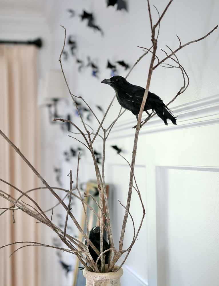 close up of fake blackbirds perched on a bare branch, colony of bats can be seen in the background, classy halloween decorating idea for simple look