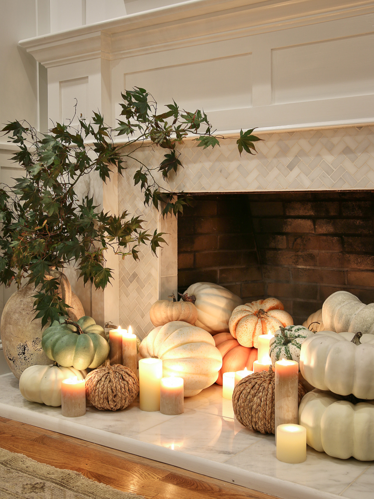 fireplace fall decor display with assorted white and pastel pumpkins, pillar candles, and vase with fall stems