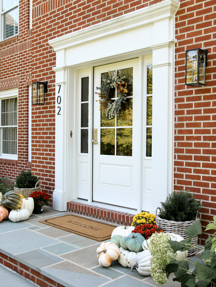 fall porch decoating ideas, brick home with bluestone porch, front door with fall wreath, porch styled with faux pumpkins, mums, planters