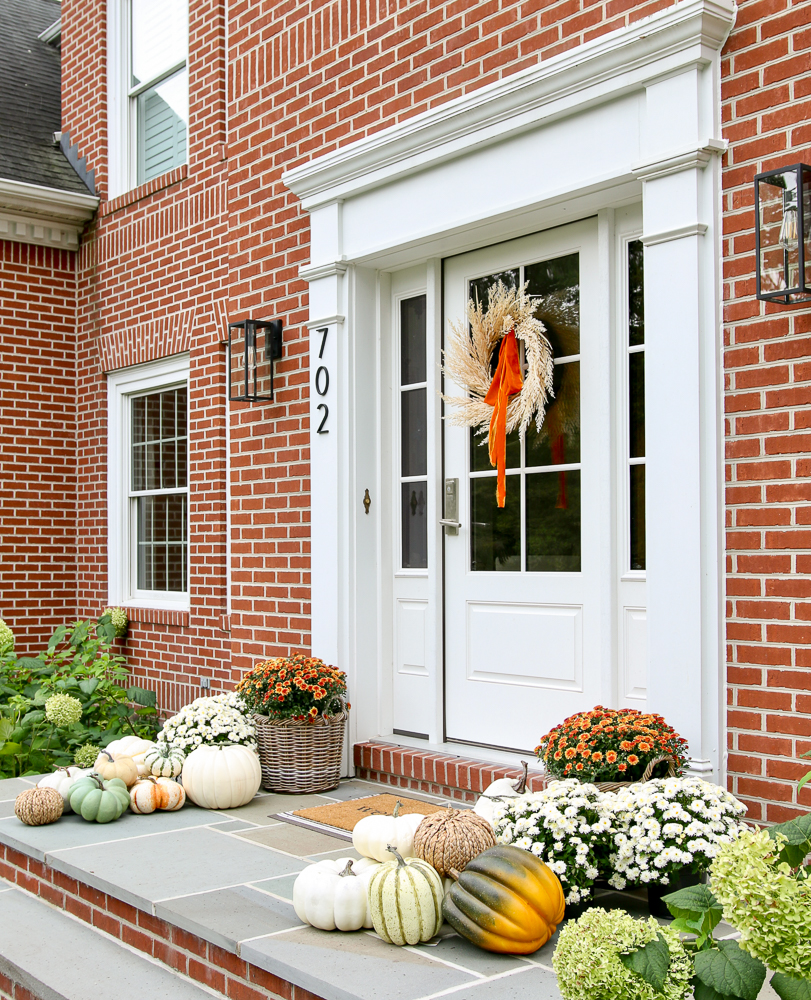 exterior of home showing fall front porch decorating ideas with wreath, faux pumpkins, fall planters with mums, and doormat