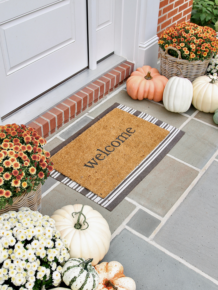 bluestone porch with decorated for fall with welcome mat, faux pumpkins and mums in rattan planters