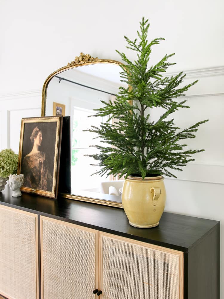 Afloral Norfolk pine small artifical tree styled on a dining room sideboard, Gleaming primrose mirror, vintage artwork, Christmas greenery, wall molding