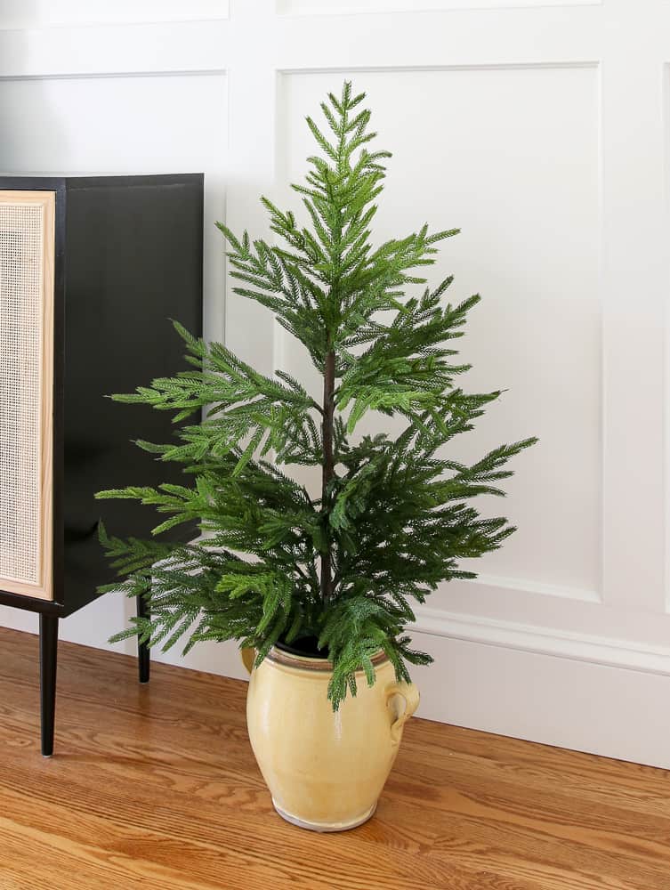 Afloral Norfolk pine small artificial tree on the floor next to the sideboard cabinet in the dining room, white walls with molding, DIY cane cabinet