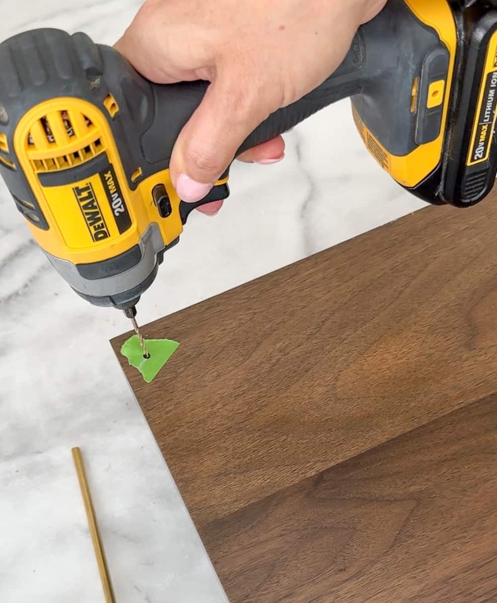 person using a cordless power drill to drill a hole in a walnut floating shelf, painters tape used to prevent splintering