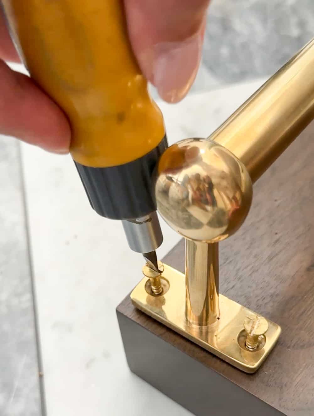 person threading screws to attach hanging brass pot rail on the underside of a walnut floating shelf 