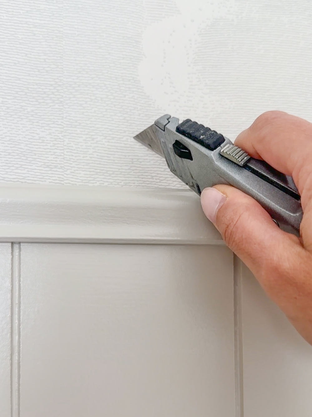 person using a utility knife to score a flap in wallpaper in order to hide the hole they are about to make