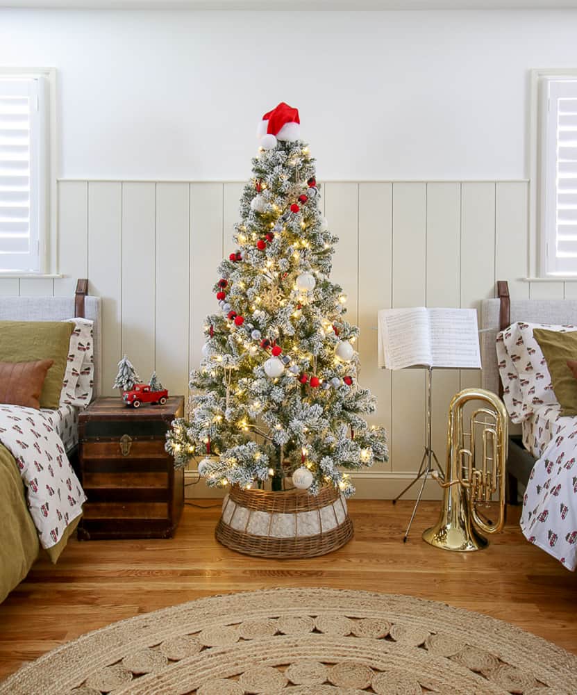 shared boys' bedroom with flocked Christmas tree, red and white decor, Christmas sheets with red truck and tree, vertical shiplap on wall behind beds, hardwood floors, music stand and tuba
