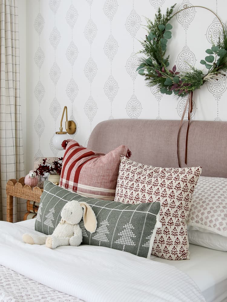 Girl's bedroom decorated for Christmas, mauve velvet unholstered bed, Serena and Lily scalloped nightstand and wallpaper, Christmas wreath above bed and pillows on bed