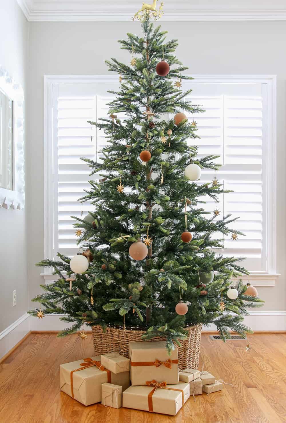 sparse Christmas tree decorated with a few velvet ornaments and gold stars, basket tree collar with wrapped gifts