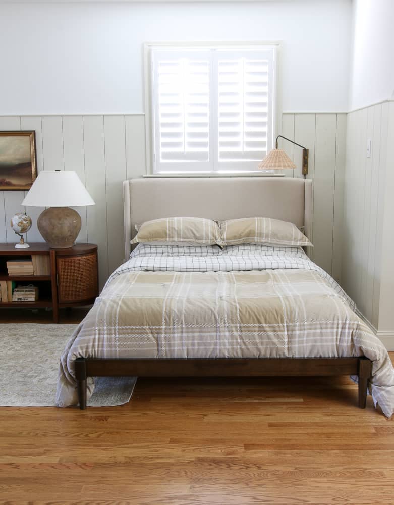 bedroom with vertical shiplap walls, hardwood floors, cane cabinet styled with bedside lamp