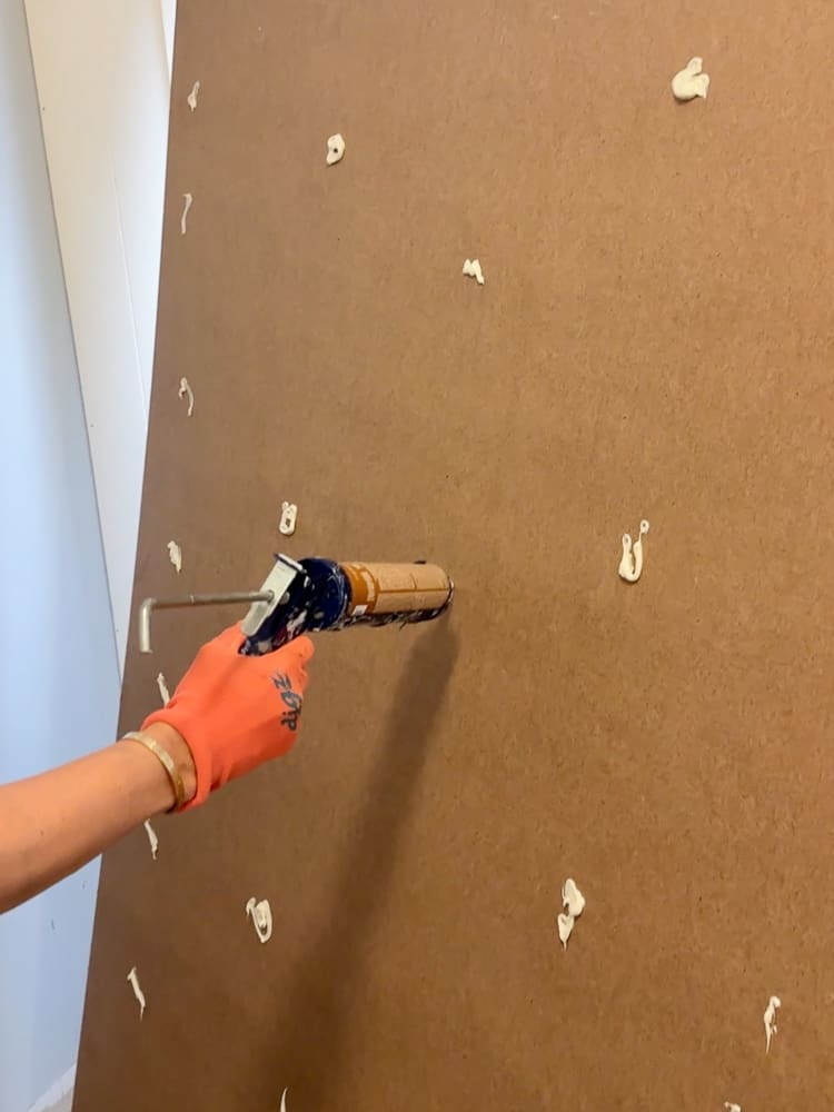 person applying construction adhesive on back of a shiplap panel prior to installing it on the wall