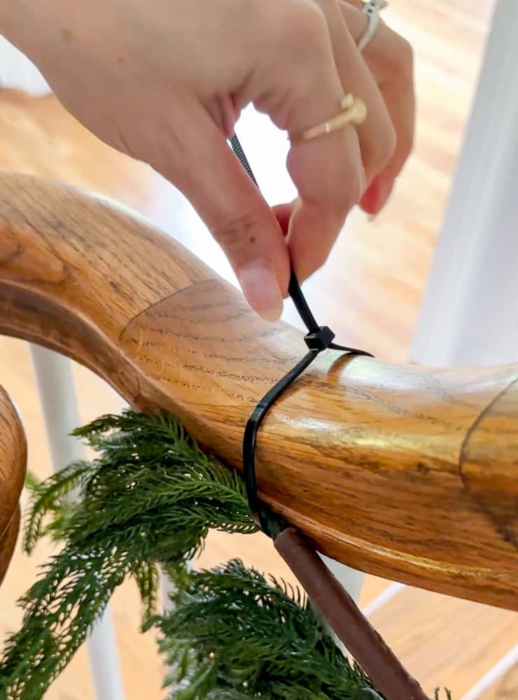 person demonstrating how use a zip tie to hang garland on a staircase