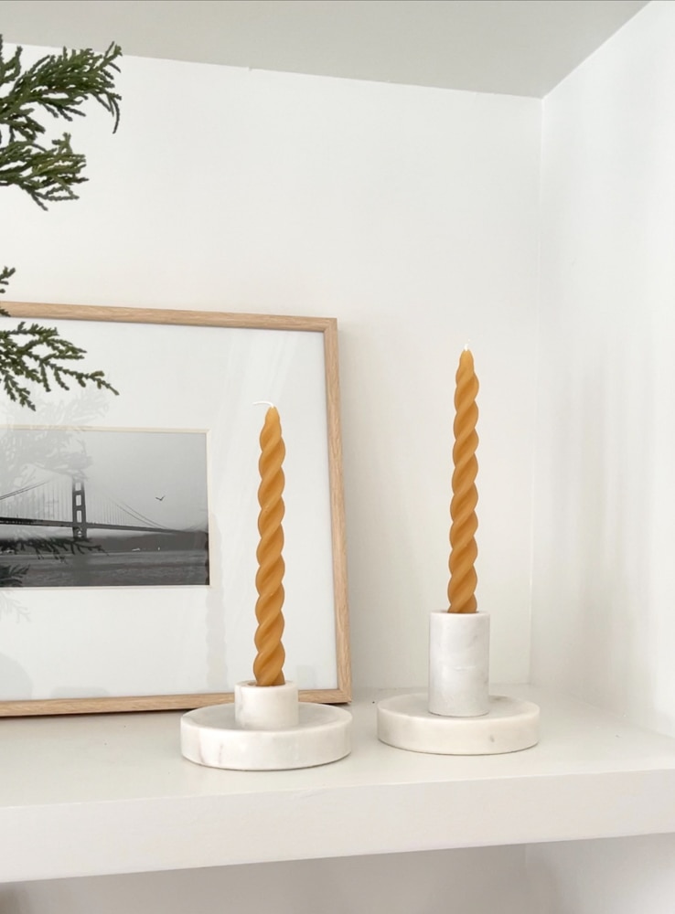 simple twisted taper candles in yellow styled in brass channel holders on built-in shelves with artwork and greenery