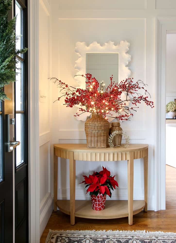 red and white Christmas decor in entryway, Poinsettias, red berry stems styled by a white mirror and wall