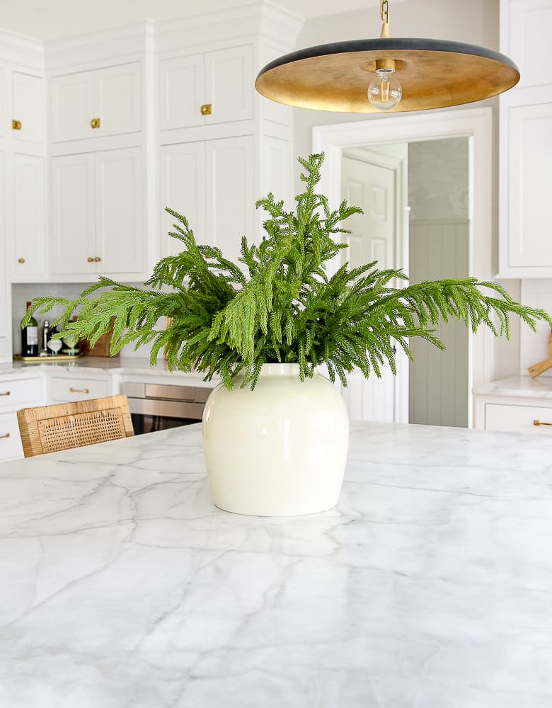 winter decorating after christmas, greenery, Norfolk pine stems styled in vase on kitchen island counter, honed marble countertops, classic white kitchen