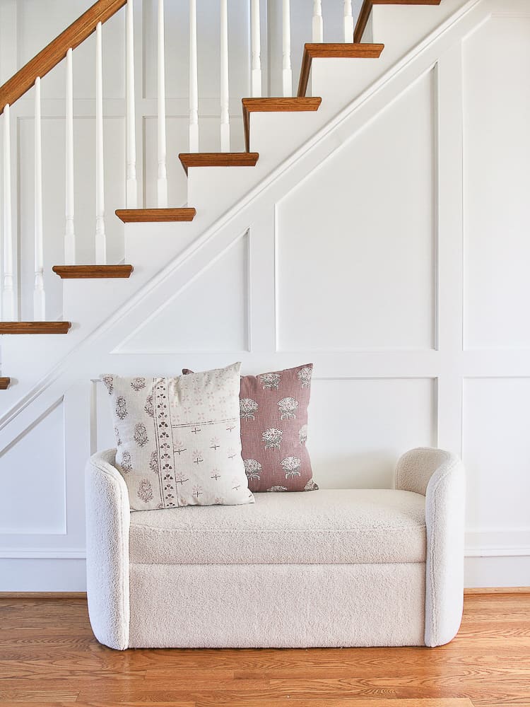 white hallway with molding, white boucle bench with throw pillows styled near stairway