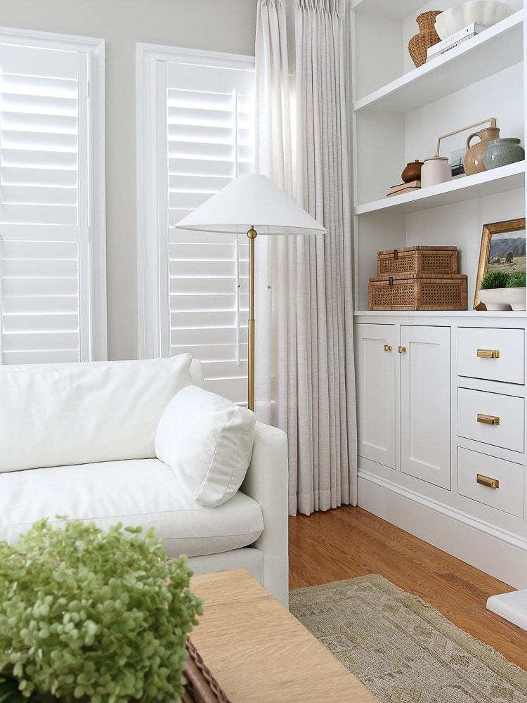 home refresh ideas for windows, corner of living room with interior window shutters and linen drapes, white velvet West Elm Marin sofa, builtin shelves and cabinets