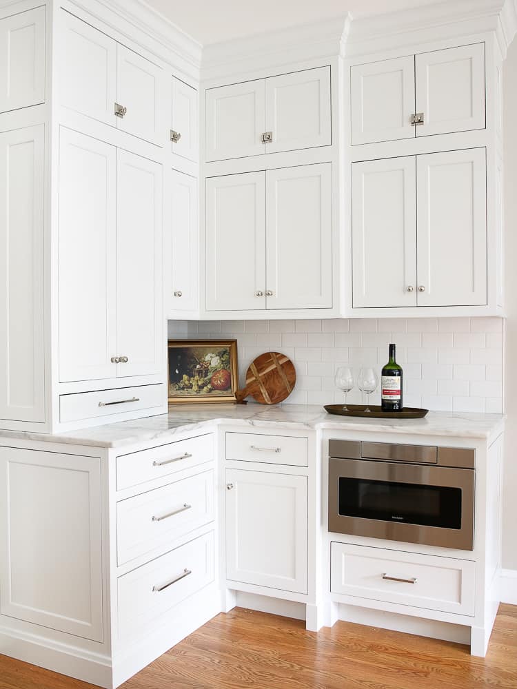 corner of classic white kitchen with Carrara marble countertops, polished nickel hardware